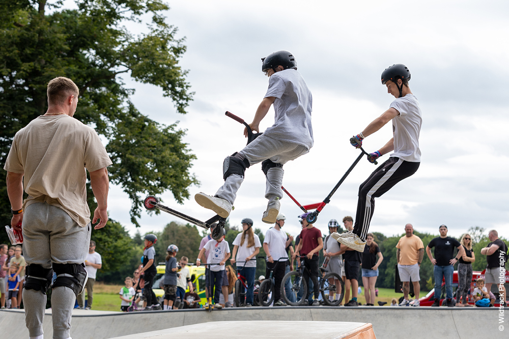 Young people enjoying Horsham Skatejam and two doing tricks on scooters