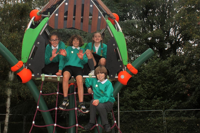 Primary school children sit at the top of Horsham Park's new play equipment smiling