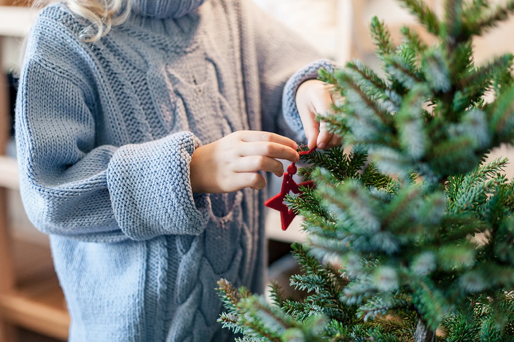 A woman in a grey jumper decorating a tree