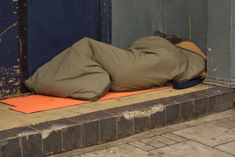 A person in a sleeping bag in a shop doorway