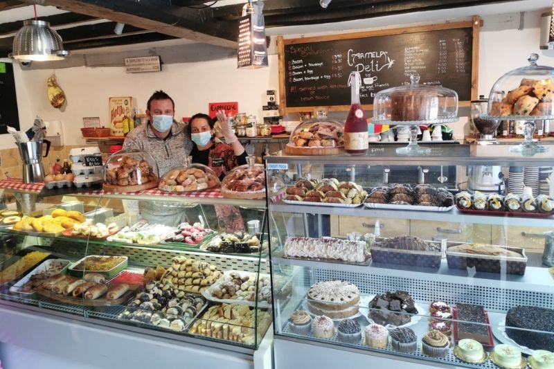 Two members of staff at Carmela Deli wear masks and wave to the camera