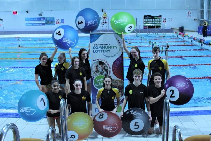 Atlantis Swimming Club members hold up Lottery signs by the side of a swimming pool